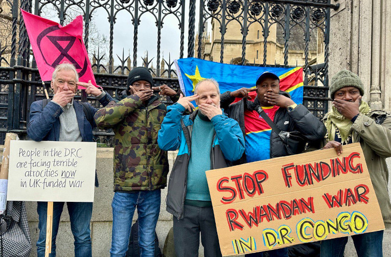 XR activists outside the UK Parliament protest the financing of violence in the DRC. The hand gesture, used by Congolese protesters to call out inaction of international and regional powers, represents being silenced with a gun to your head.