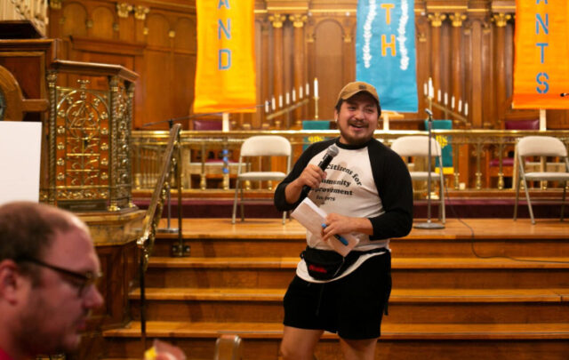 Jamie Izaguirre speaking at the Dubuque People’s Housing Forum held in St. Lukes United Methodist Church on October 1, 2023 . The banners in the background, made by Iowa Citizens for Community Improvement members in Dubuque, read “Stand with Tenants.” (Karla Conrad)